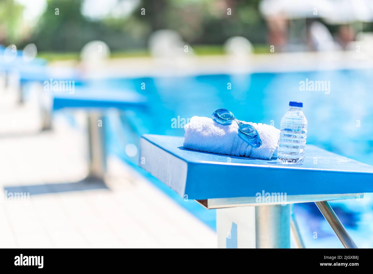 Swimming goggles, towel and water bottle placed on the starting bridge by the swimming pool. Stock Photo