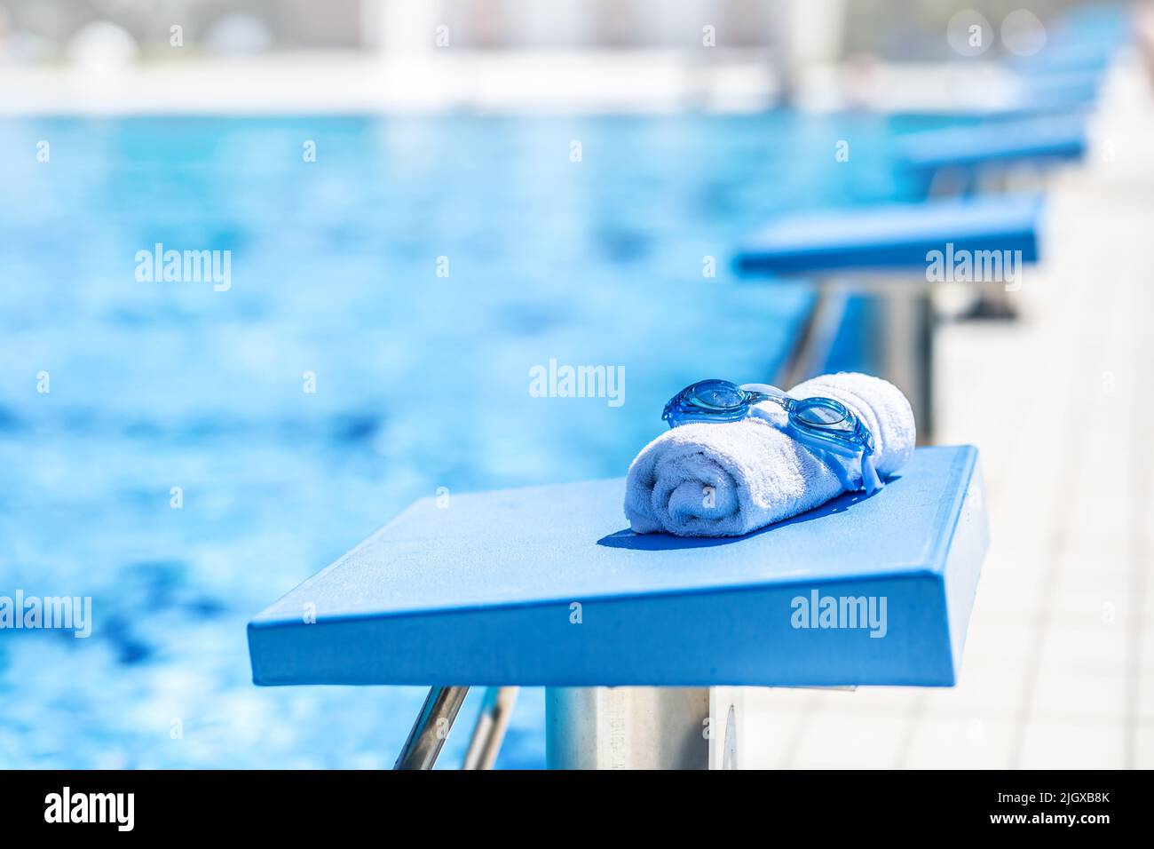 Swimming goggles and a towel placed on the starting bridge by the swimming pool. Stock Photo