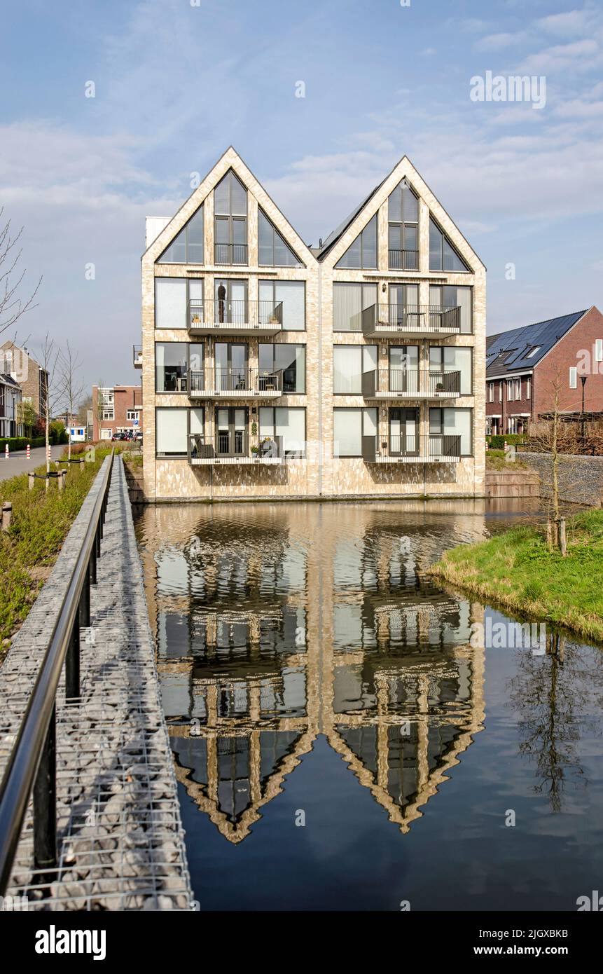 Middelharnis, The Netherlands, March 30, 2022: house-shaped apartment building with brick and glass facade, reflecting in a pond Stock Photo