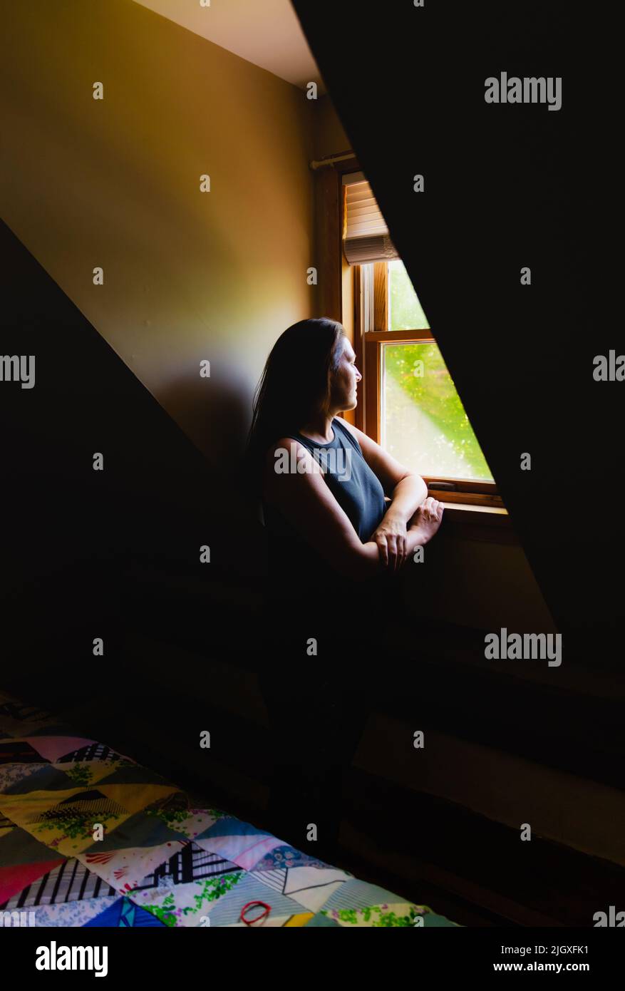 Woman looking out of a window in a dark room in the daytime. Stock Photo