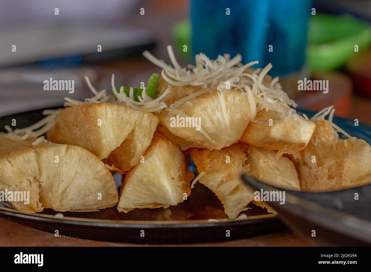 Fried Cassava with cheese sprinkles served on a black ceramic plate, a snack for lunch Stock Photo