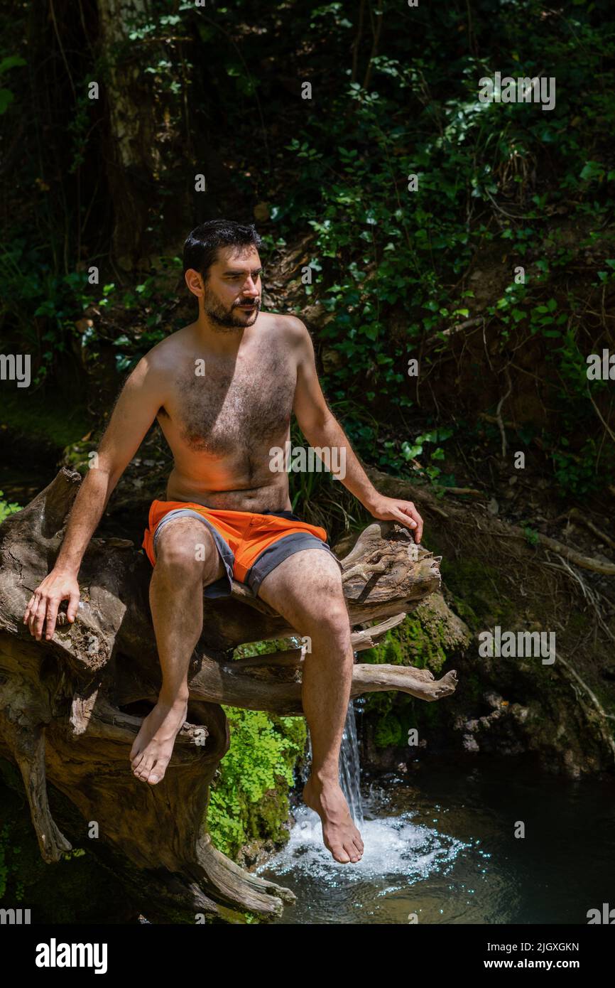 young man in swimsuit sitting in a tree by the river Stock Photo