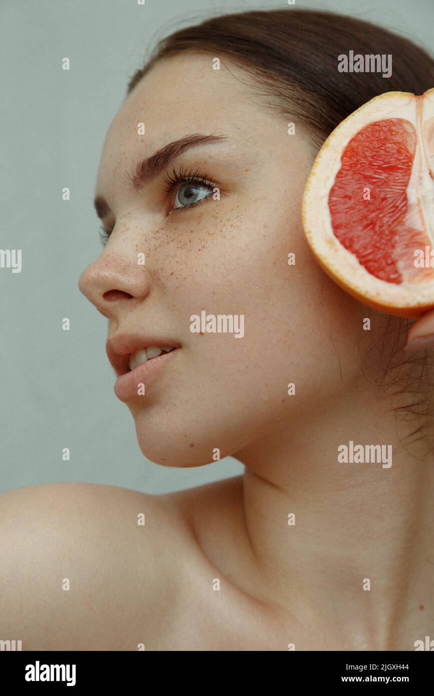 Close-up portrait of a young woman with freckles and half a grapefruit Stock Photo