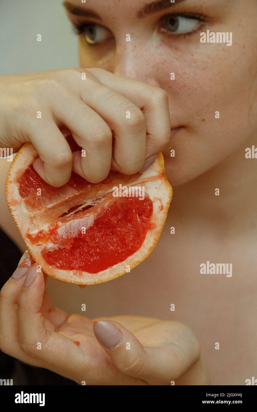 Young woman squeezes grapefruit juice with fingers. Close-up portrait Stock Photo