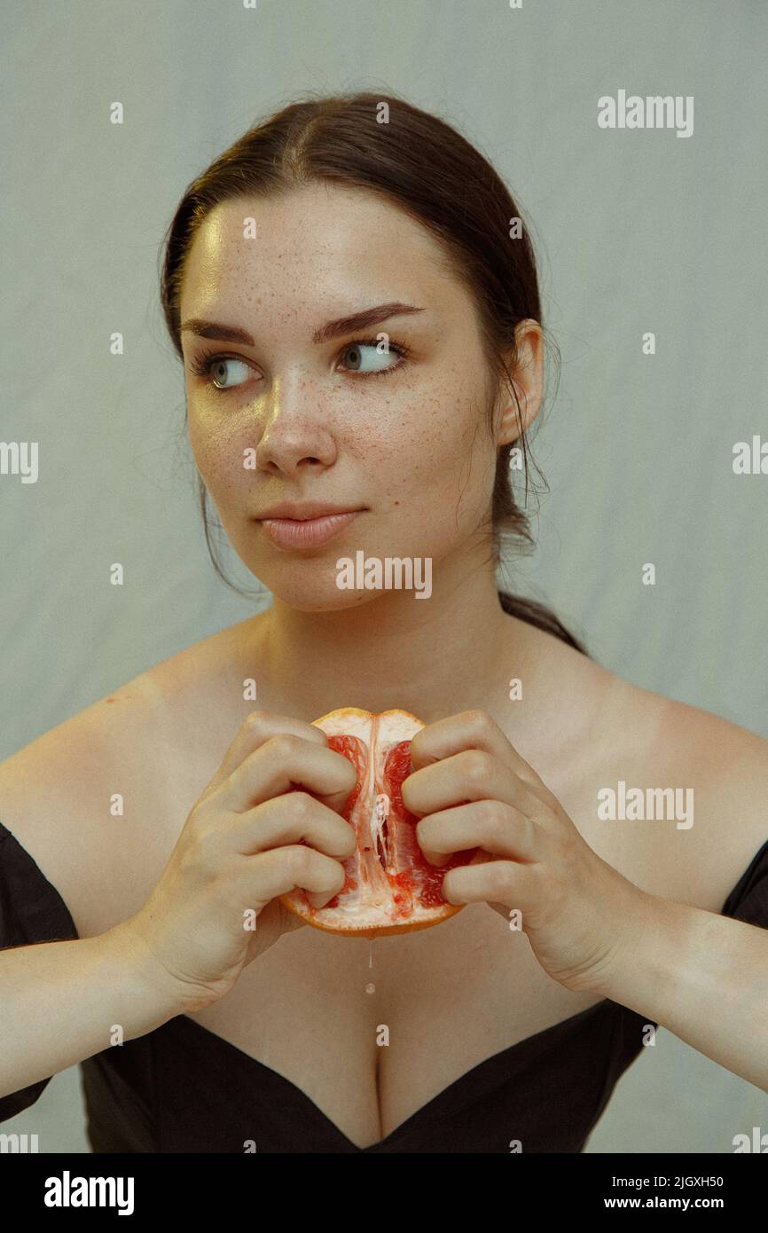 A young woman with freckles squeezes grapefruit juice with her fingers Stock Photo