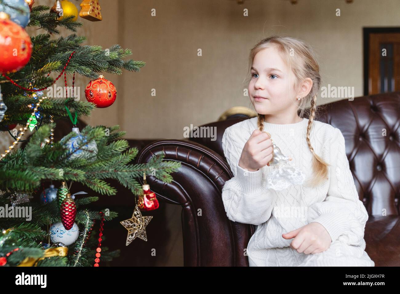 A girl with a Christmas tree toy near a festive Christmas tree. Stock Photo
