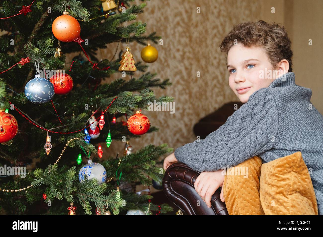 Portrait of a beautiful 11-year-old boy near the Christmas tree. Stock Photo