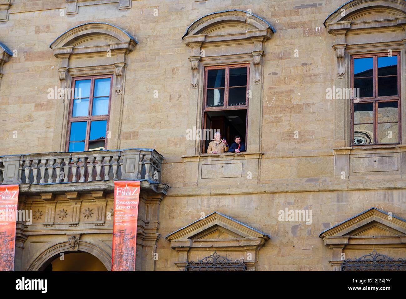 Two men look out of a window of the Franco Zeffirelli Foundation building at a Palm Sunday religious processional, Florence, Italy. Stock Photo