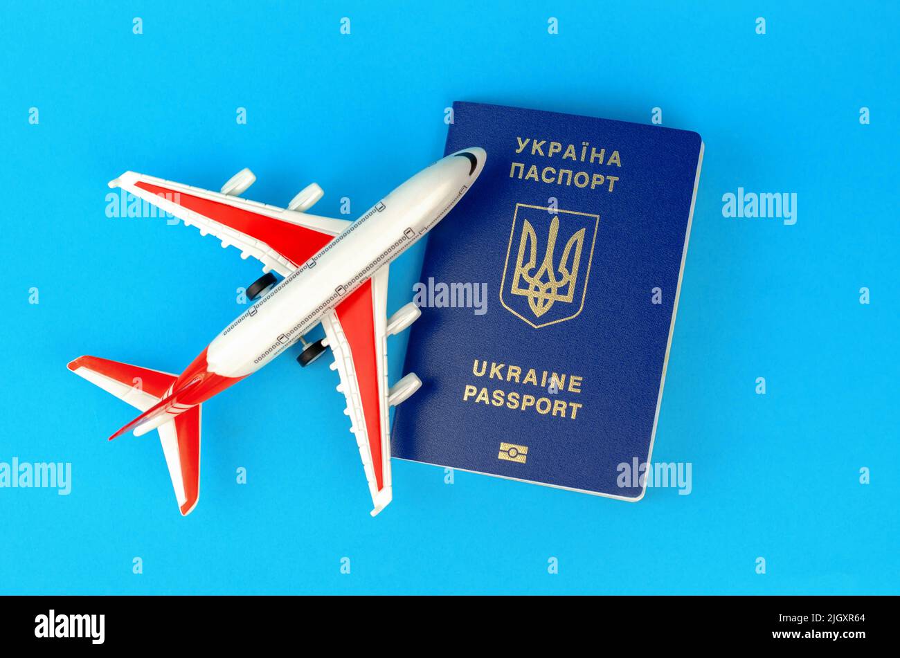 Ukrainian biometric passport and toy plastic plane on a blue background. Departure of Ukrainians abroad Stock Photo