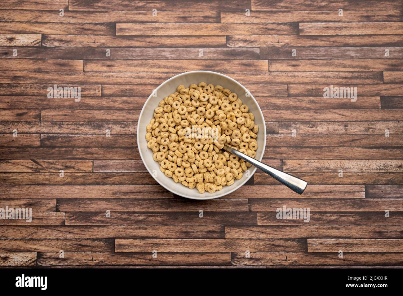 Cereals in a white bowl with a spoon on a wooden table. Round cornflakes for breakfast. Looking down from above. Delicious wheat loops are a snack. Stock Photo