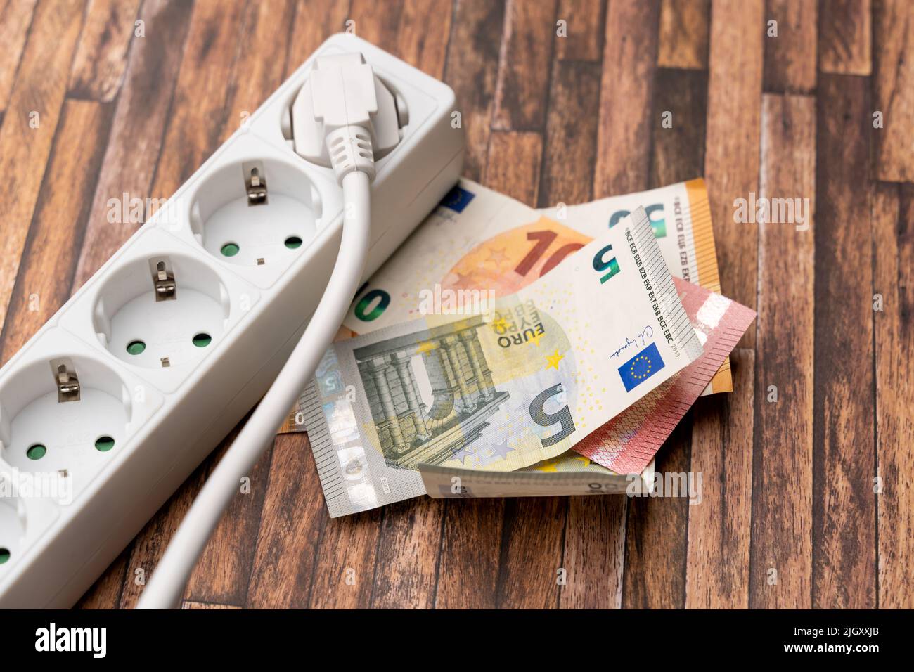 Euro banknotes next to a power socket. Symbolic image for a high electricity price. Increasing energy costs due to inflation effects. Multi socket Stock Photo