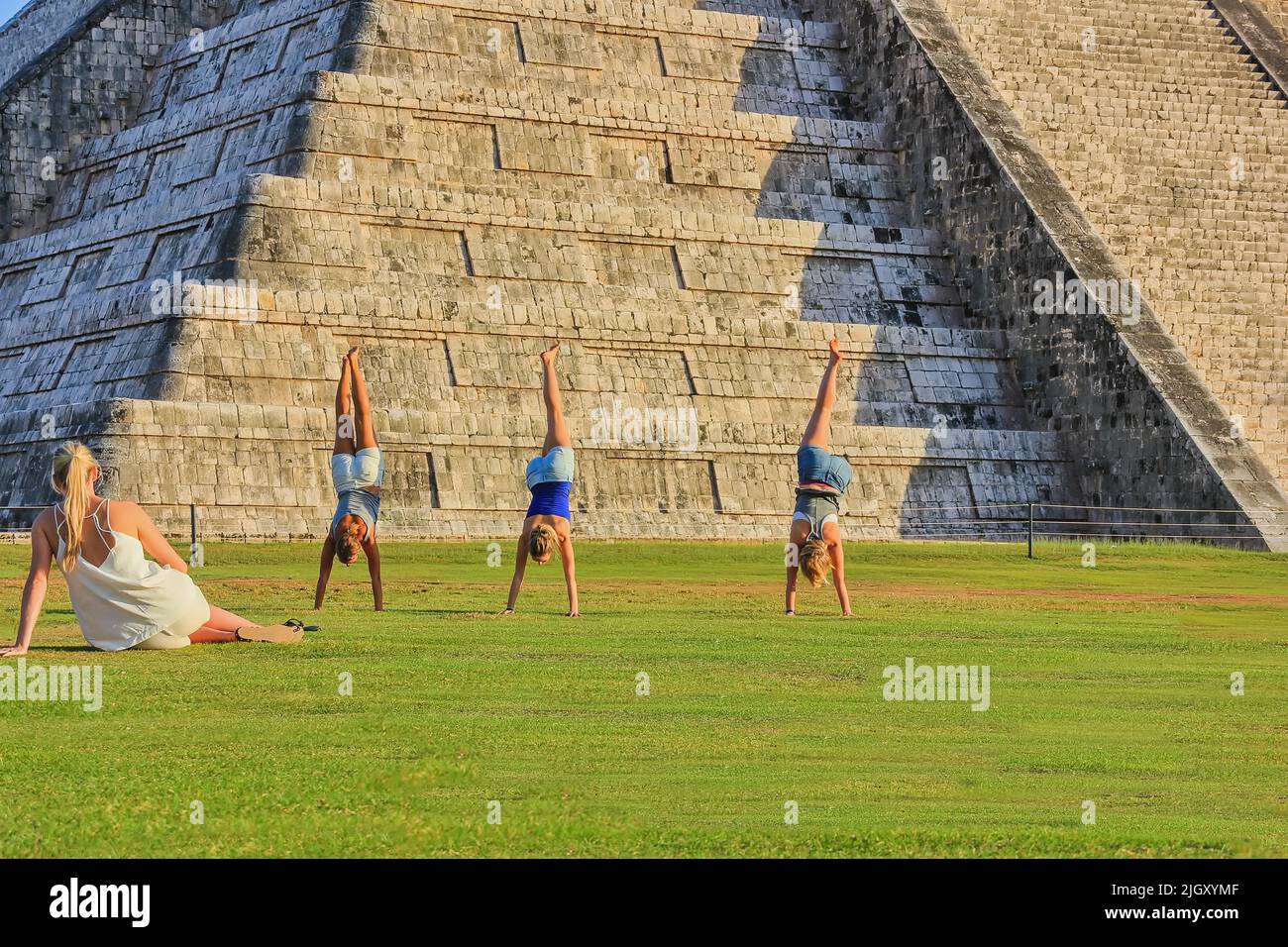 Rear view to group of three young girls posing handstand against the main Mayan civilization ruin is the Chichen Itza Pyramid Stock Photo