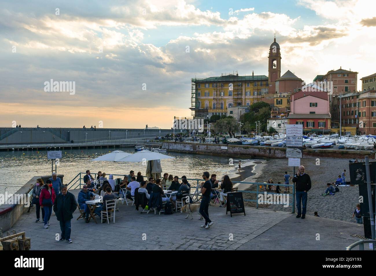 View of the ancient fishing village with people at waterfront cafè and the small port in springtime at sunset, Nervi, Genoa, Liguria, Italy Stock Photo