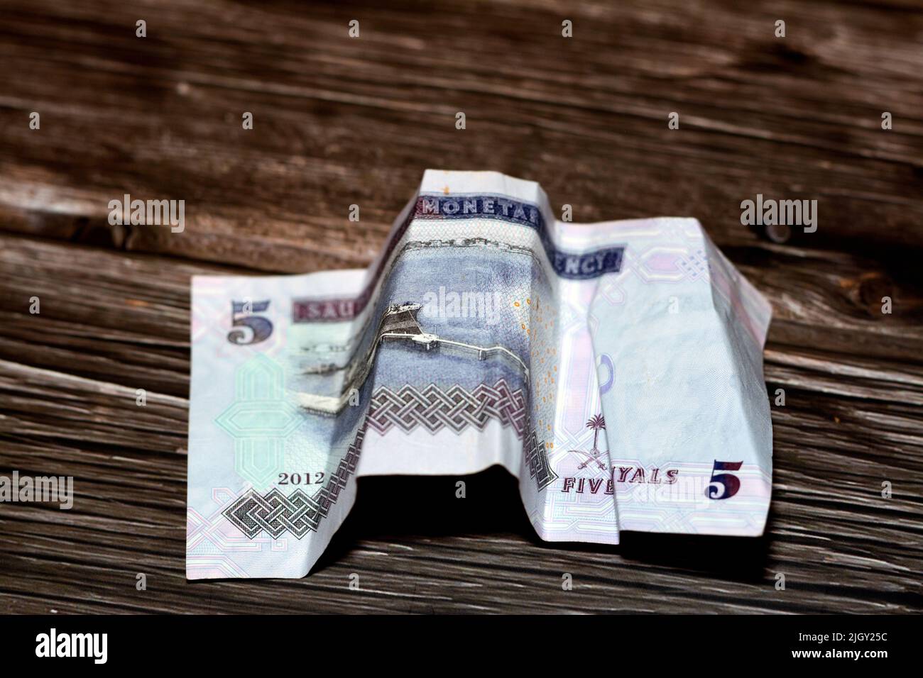 Crumpled Saudi Arabia money of 5 SAR five riyals isolated on wooden background, wrinkled 5 Saudi Riyals cash bill banknote, Saudi money inflation and Stock Photo