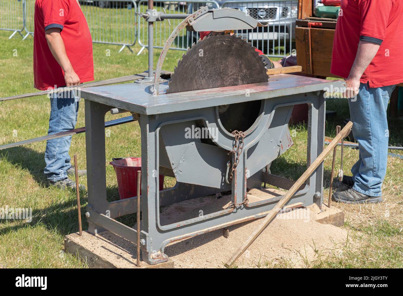 Two males in red shirts standing by a circular saw in the outdoors Stock Photo