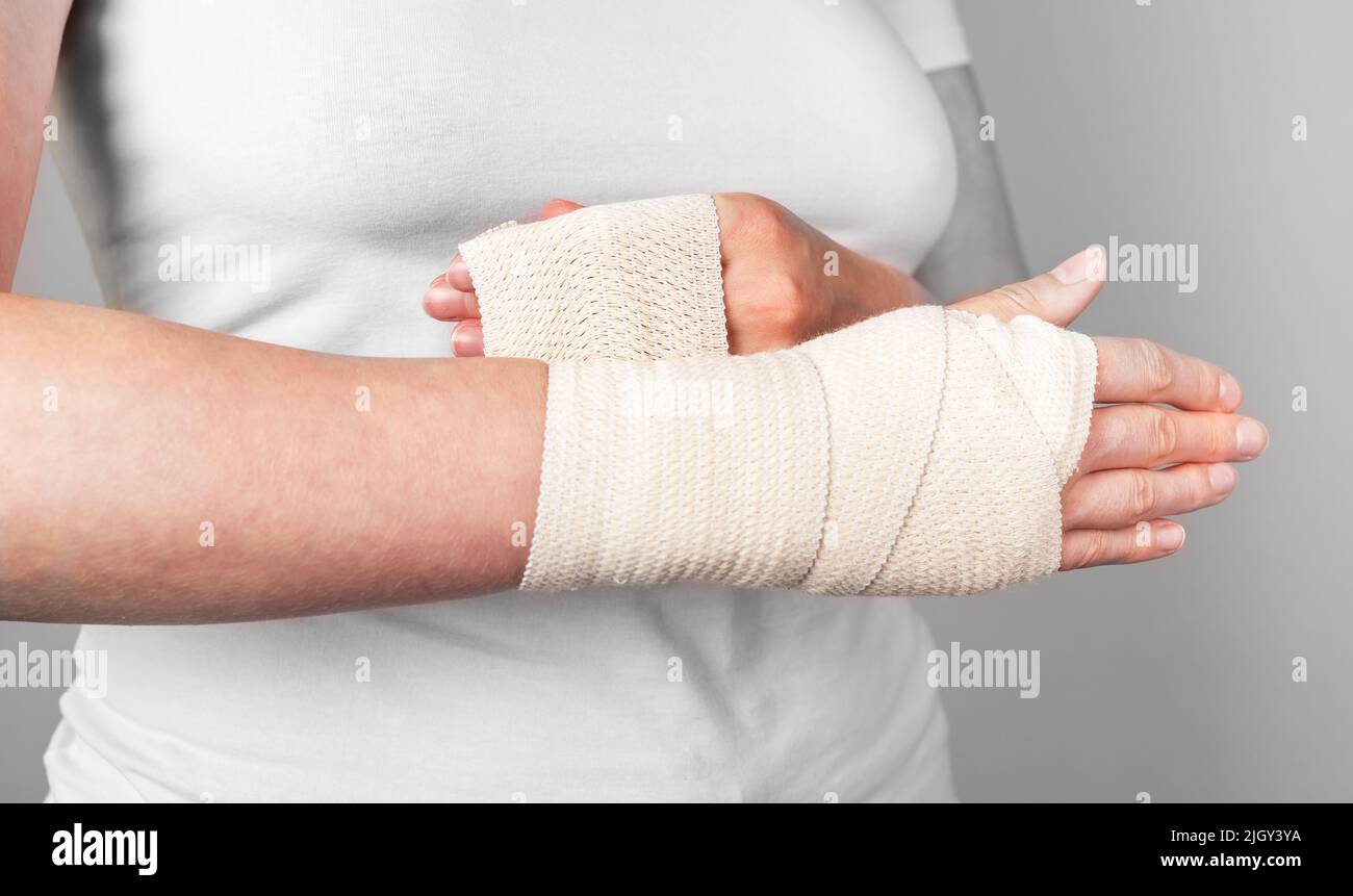 Young woman herself is bandaging upper limb. Bandaging a wrist wound with a  gauze bandage Stock Photo