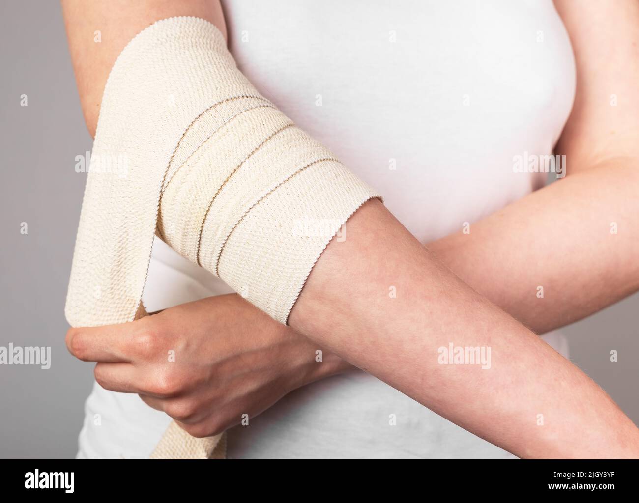 Woman wrapping compression bandage around painful elbow to relieve pain or prevent injury. Muscle sprains, strains, overuse treatment. Arm trauma. Health care concept. High quality photo Stock Photo