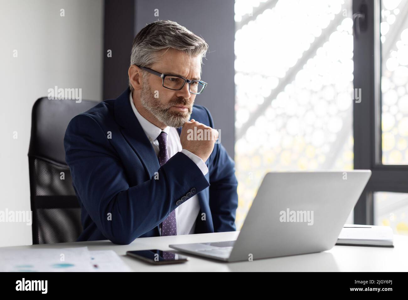 Focused Middle Aged Businessman Looking At Laptop Screen While Working In Office Stock Photo