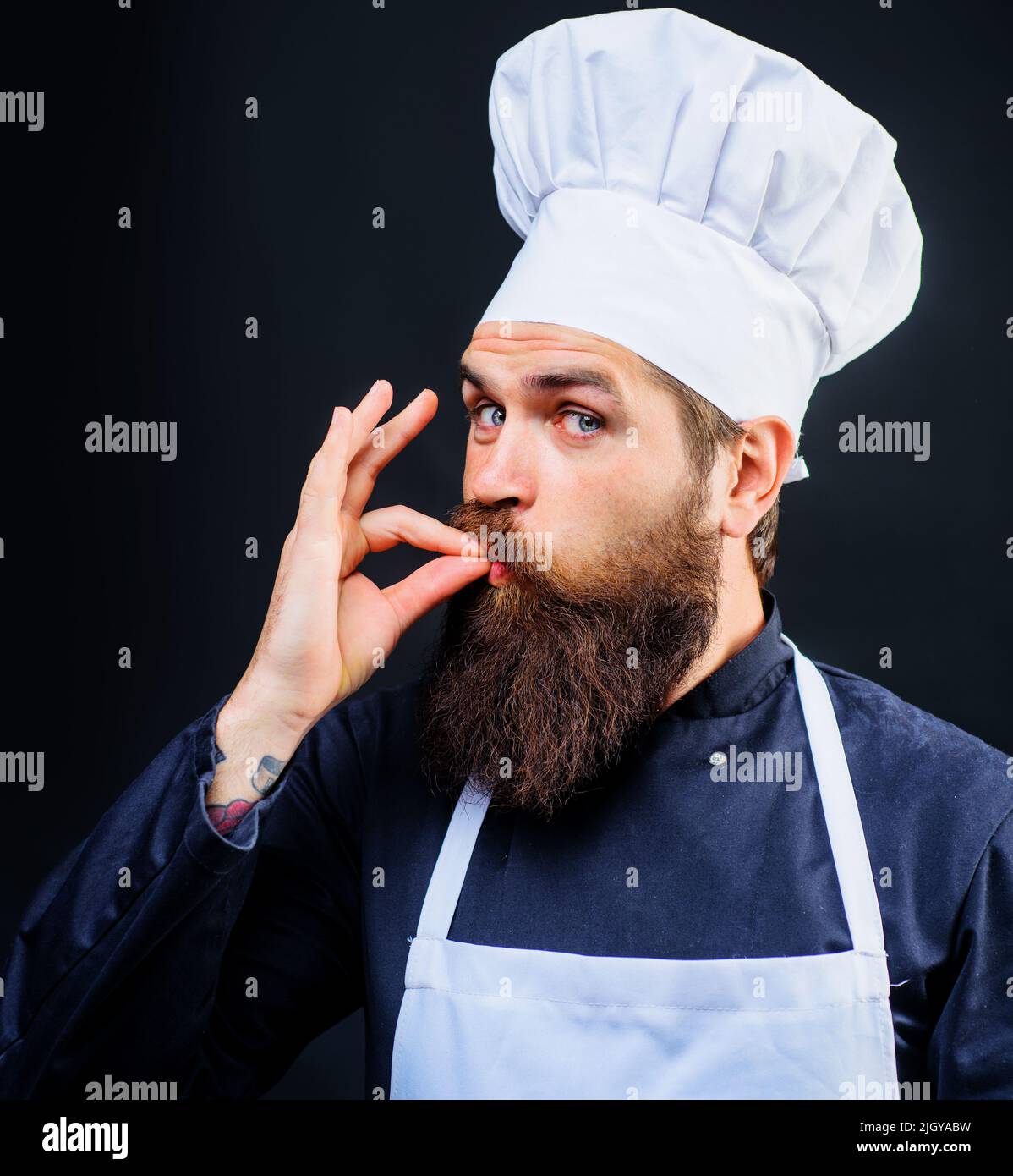 Male chef or baker in white hat and apron gesturing excellent. Cook with taste approval gesture. Stock Photo