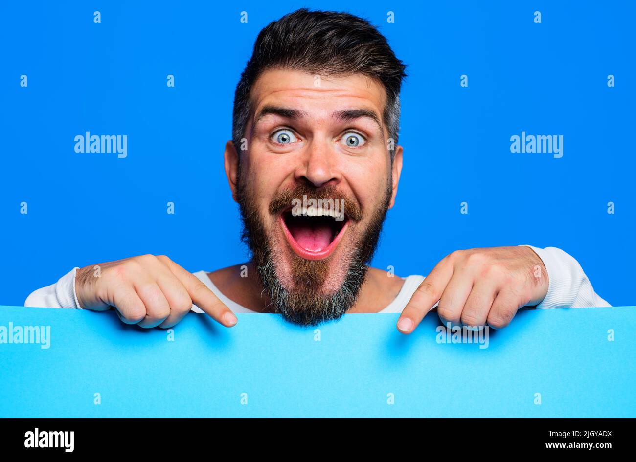 Happy man presenting empty advertising banner. Bearded guy shows blank sign board. Stock Photo