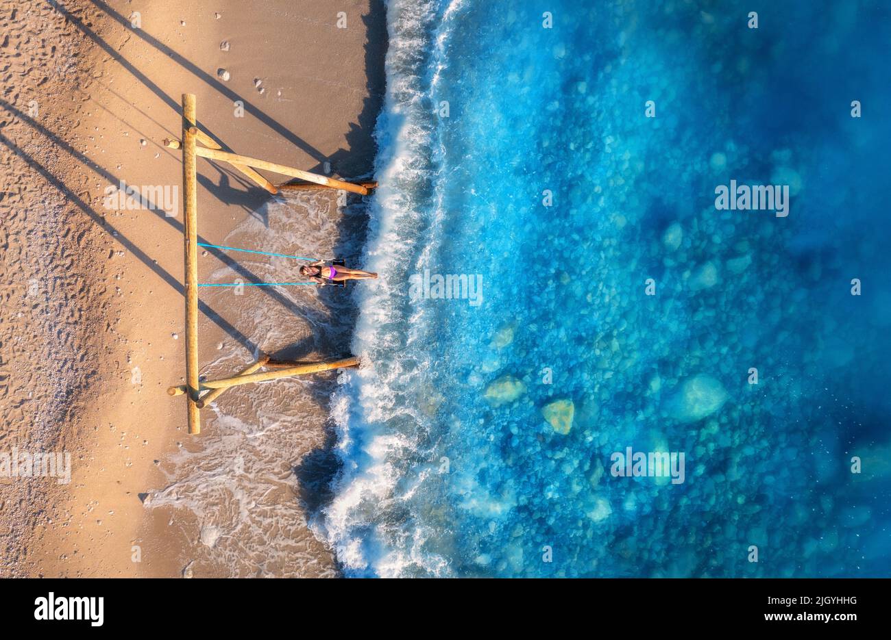 Aerial view of woman on the swing, beautiful blue sea with waves Stock Photo