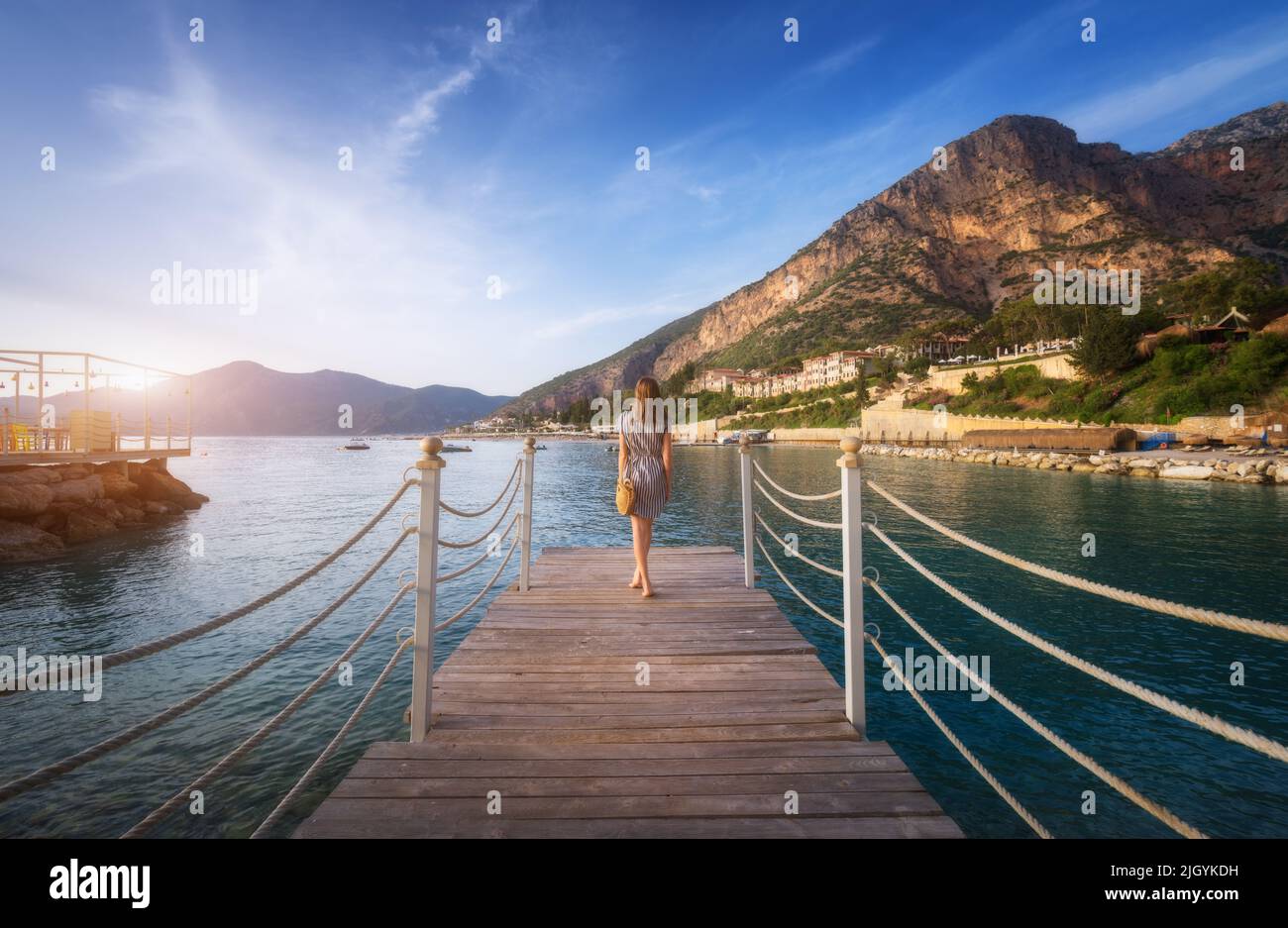 Young woman on wooden pier on sea shore is looking on mountain Stock Photo