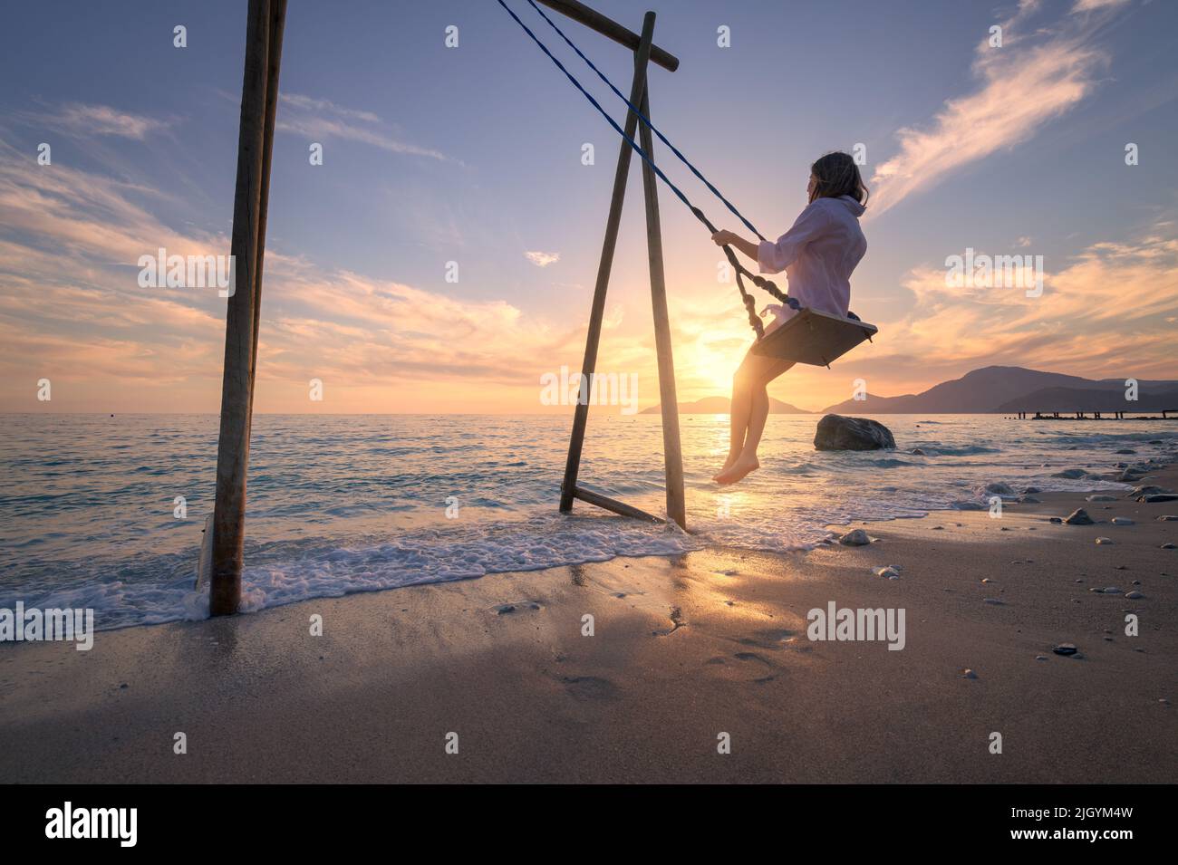 Happy young woman on wooden swing in water, sea with waves Stock Photo