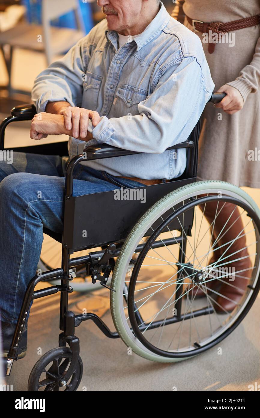 Close-up of unrecognizable woman in dress pushing man in wheelchair while taking care of seniors in nursing home Stock Photo