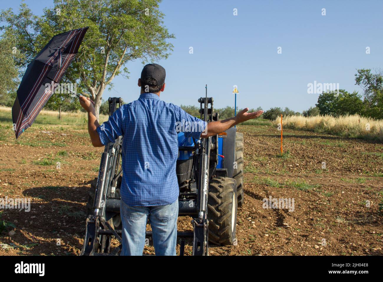 Image of a farmer with umbrella in the middle of a field looking up at the sky. Reference to climate change and the lack of rain and water in crops. Stock Photo