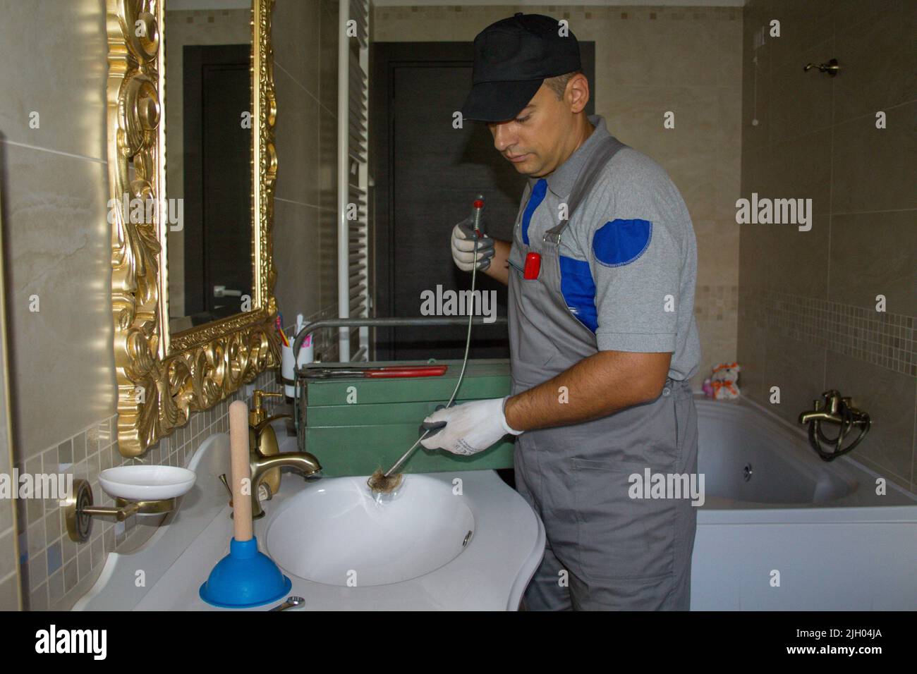 Image of a smiling plumber who unclogged a clogged sink with a probe. Do-it-yourself work Stock Photo