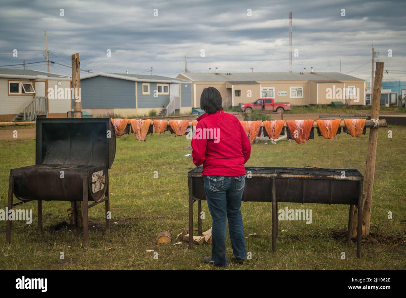 Woman monitoring the fillets of Lake Trout being smoked above fire in the northern Indigenous community of Deline, Northwest Territories, Canada. This Stock Photo