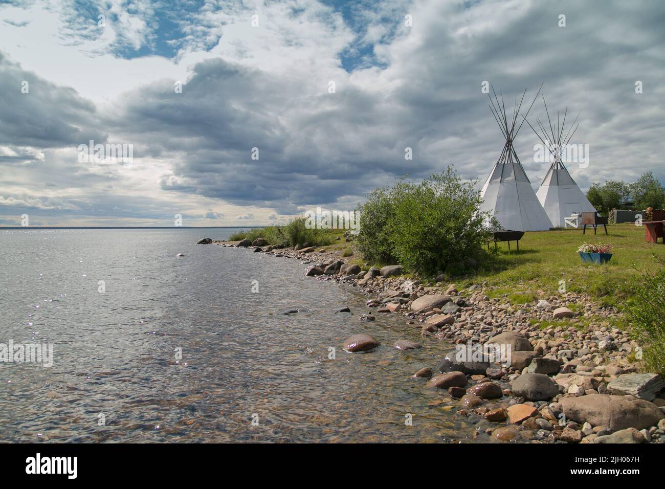 Shoreline of Great Bear Lake in summer, with teepees in the distance, in the northern Indigenous community of Deline, Northwest Territories, Canada Stock Photo