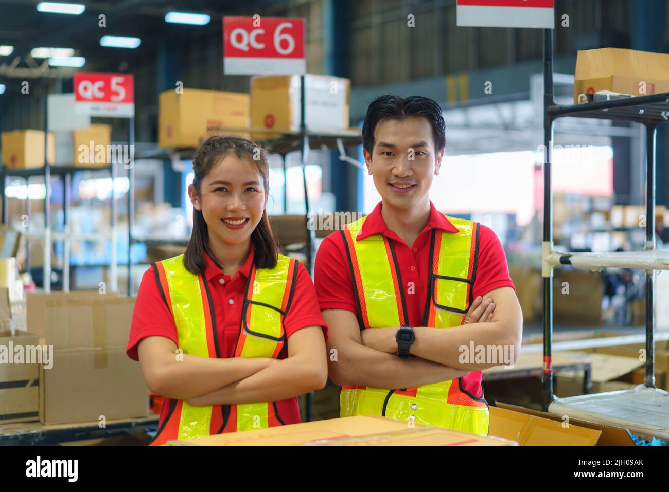 Asian couple warehouse worker smiling and arm cross at counter already preparation container box goods deliverly to customer. Stock Photo