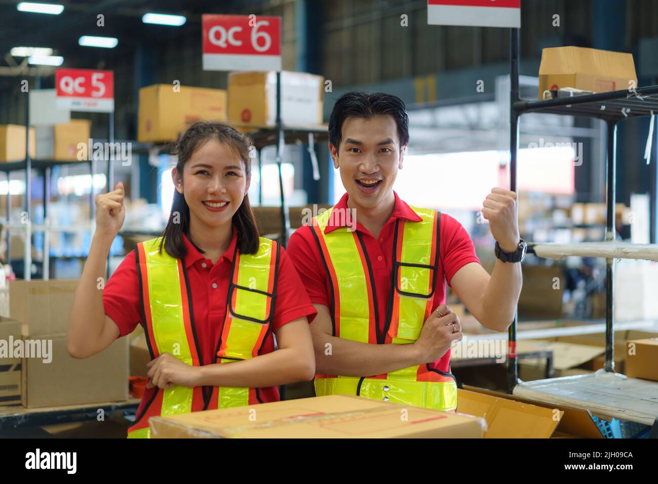 Asian couple warehouse worker smiling and arm raised at counter already preparation container box goods deliverly to customer. Stock Photo