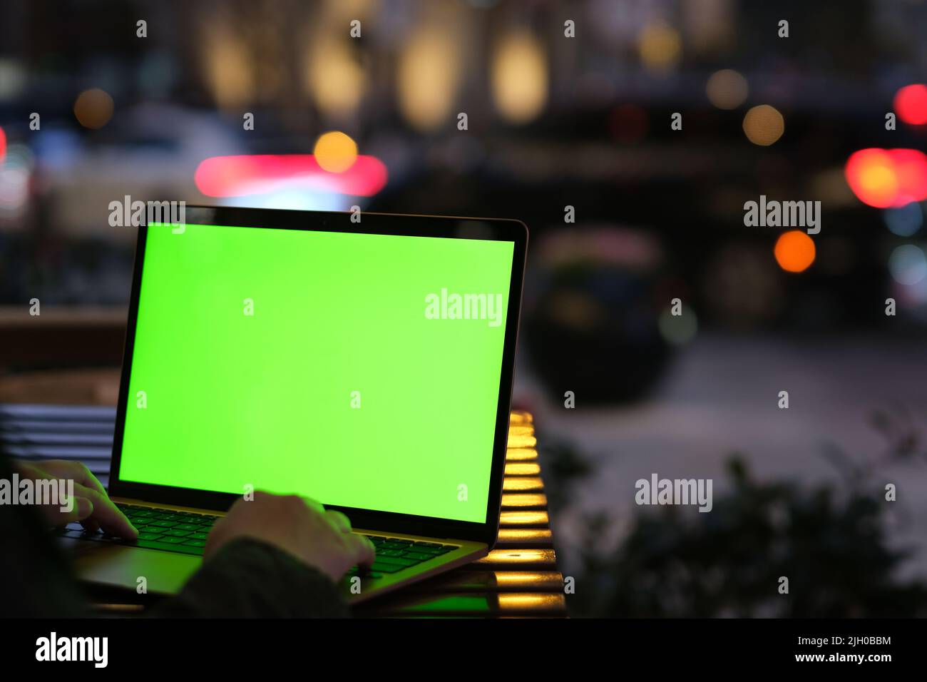 over the shoulder of people typing green screen laptop computer at night cafe. Stock Photo