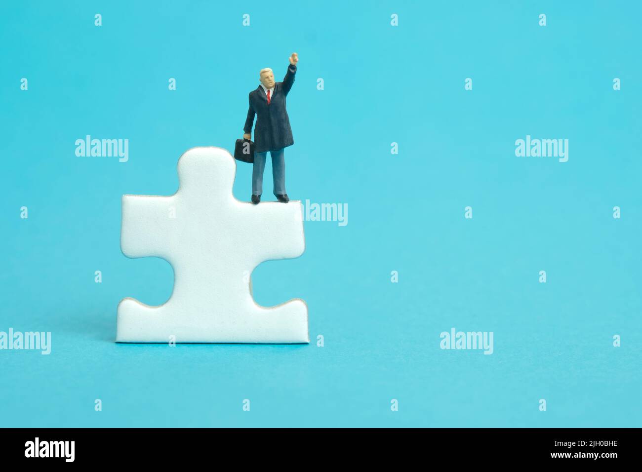 Miniature people toy figure photography. A businessman standing above puzzle jigsaw piece while raise his hand. Isolated on blue background. Image pho Stock Photo
