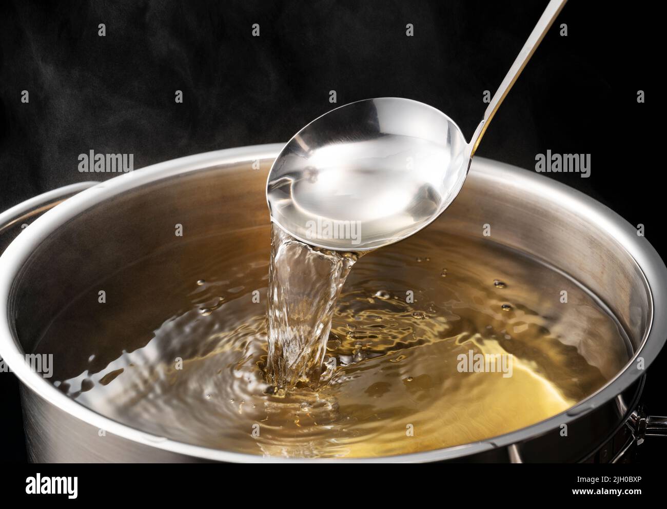 Dashi, soup stock, and the basics of Japanese cuisine. Black background. Steam. Scooping with a ladle. Stock Photo