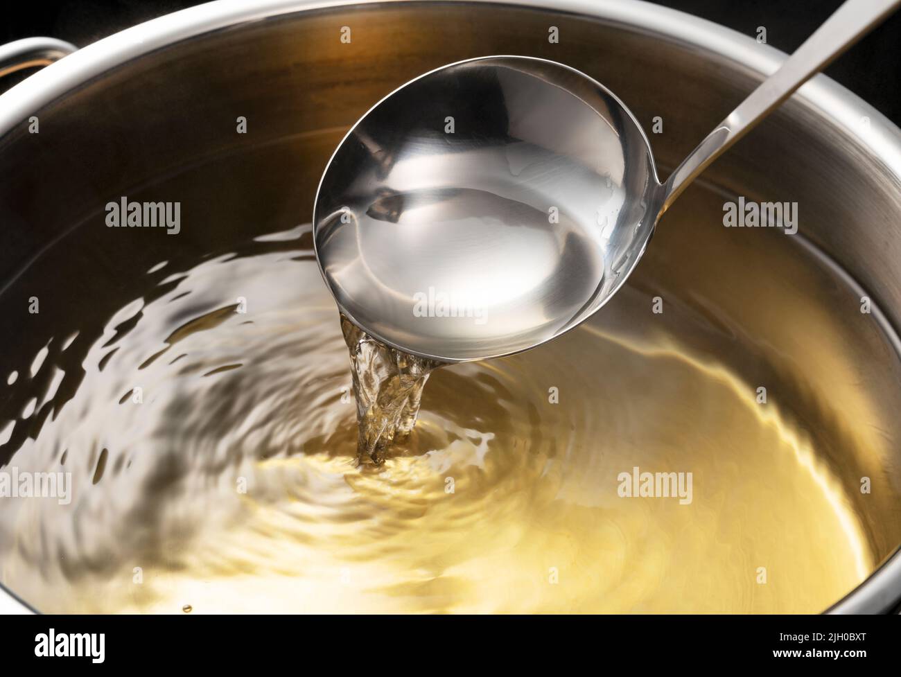 Dashi, soup stock, and the basics of Japanese cuisine. Black background. Steam. Scooping with a ladle. Stock Photo