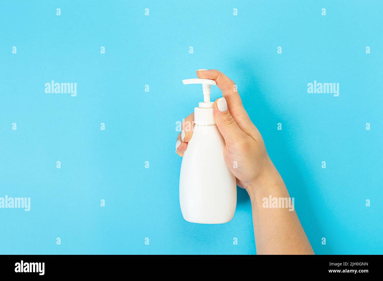 Housewife's hand holds a spray with cleaning agent on a blue background