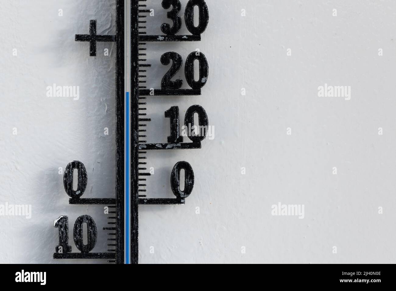 Classic black analog thermometer hanging on white wall displaying blue temperature scale of twenty, 20 degrees celsius Stock Photo