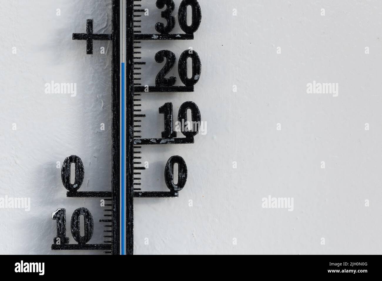 Classic black analog thermometer hanging on white wall displaying blue temperature scale of twenty-five, 25 degrees celsius Stock Photo