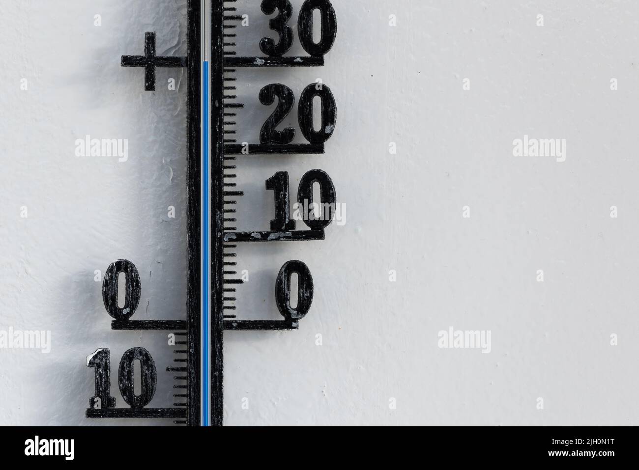 Classic black analog thermometer hanging on white wall displaying blue temperature scale of thirty, 30 degrees celsius Stock Photo