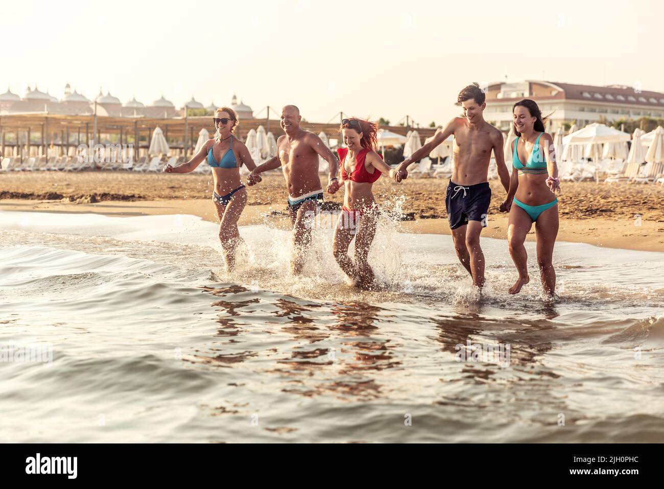 A family of five enjoys vacation by the sea. Hand in hand they run from the sandy beach to the sea. Stock Photo