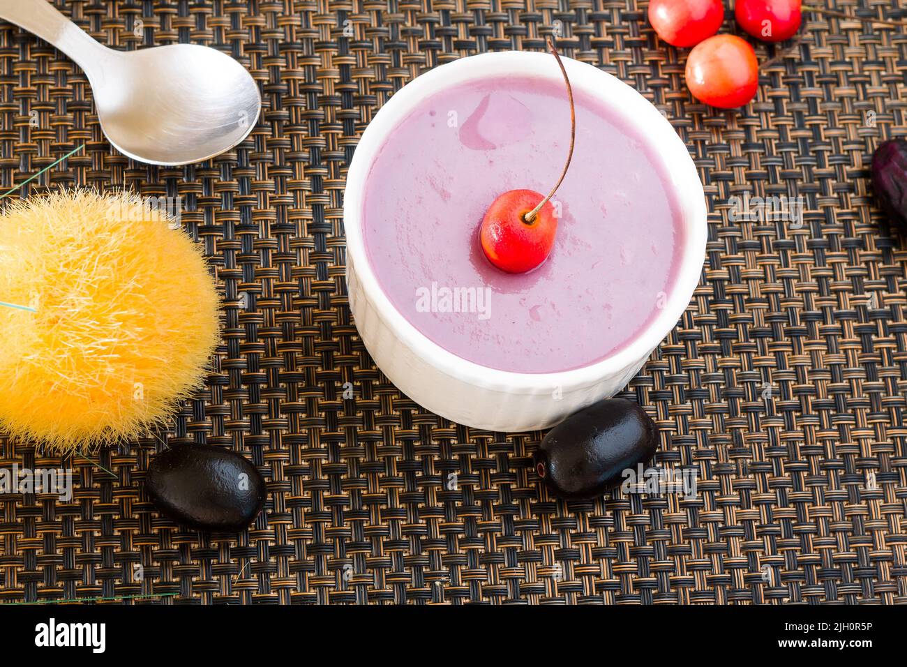 Jamun Mousse or Black Plum Mousse topped with cherries.Fresh,homemade vegan dessert.Top view,closeup of bowl isolated on dark background.Copy space. Stock Photo