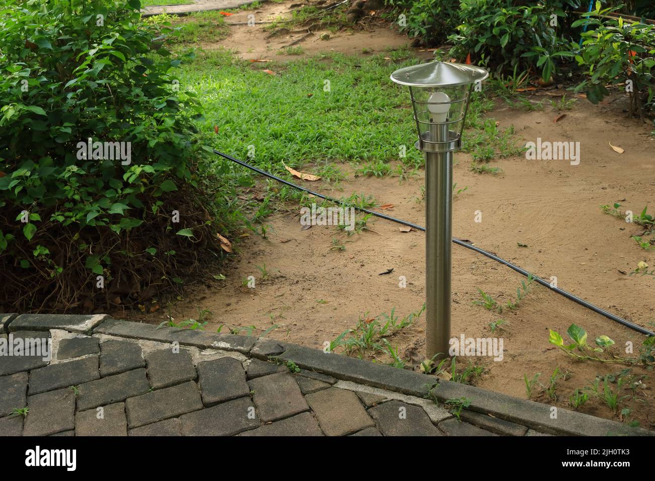 Modern style silver colored lamp post with LED energy saving bulb installed in garden next to walkway Stock Photo