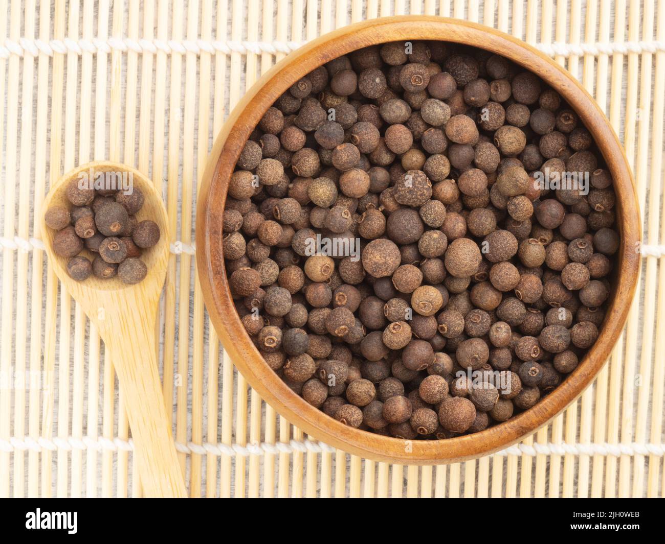 Spice Allspice (Jamaica pepper, Pimento) in wooden bowl and spoon on background of tied wooden