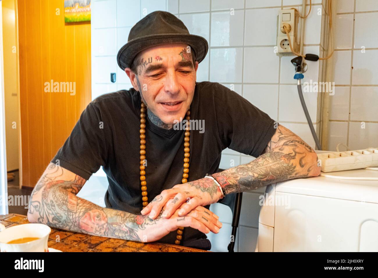 Tilburg, Netherlands. Portrait of a middle aged man with an abundance of tattoos having tea inside his vintage kitchen. Stock Photo