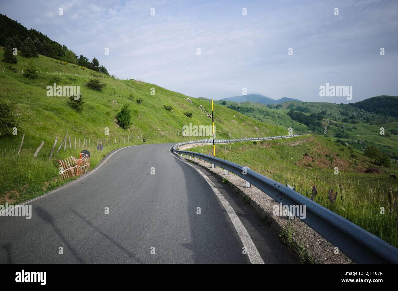 Winding asphalt road with traffic barrier an without median strip in Apennines, Liguria, Italy. Mountain road among green hills. Scenic landscape Stock Photo