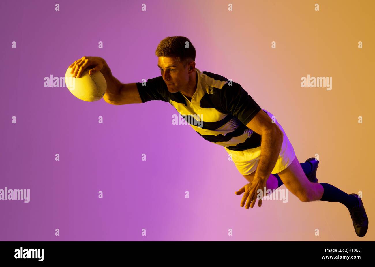 Caucasian male rugby player jumping with rugby ball over pink lighting