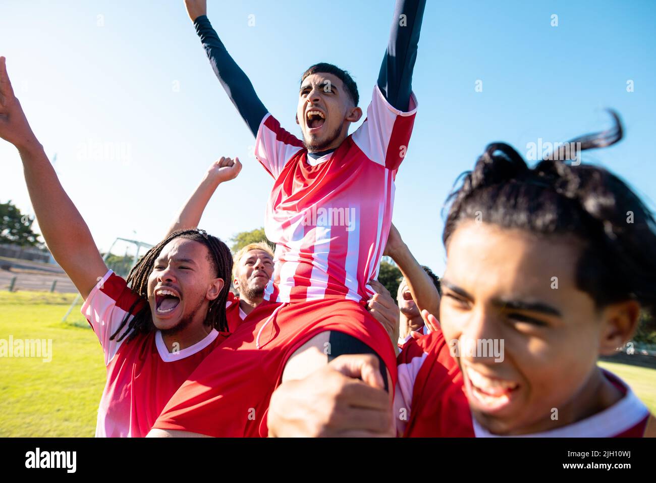 Multiracial male players carrying cheerful teammate on shoulders screaming while celebrating goal Stock Photo